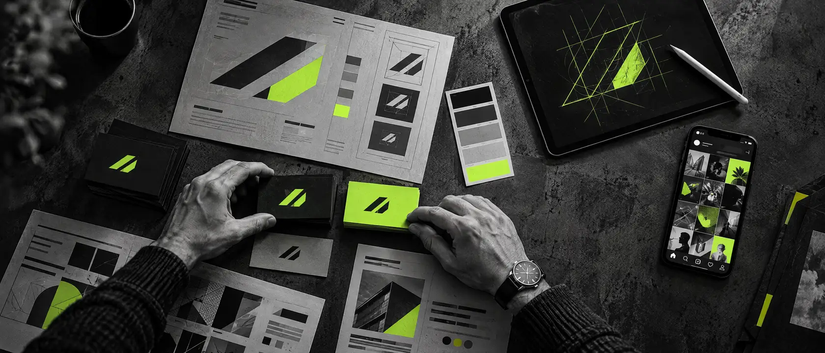 Mesa de diseño vista desde arriba con tarjetas de presentación, manual de marca, muestras de color y una tableta con un boceto de logo en verde lima